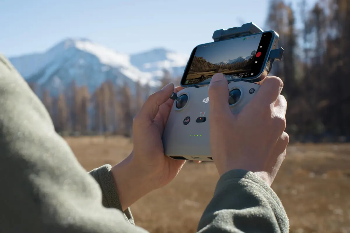 DJI Flip, Osoba steruje dronem DJI Flip za pomocą aplikacji na smartfonie, w tle ośnieżone góry