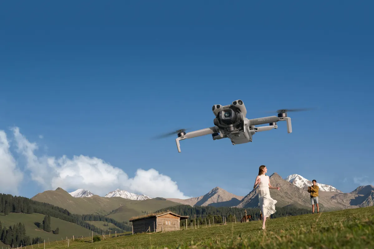 DJI Mini 5 Pro, DJI Mini 5 Pro podczas lotu nad łąką, w tle osoby sterujące dronem