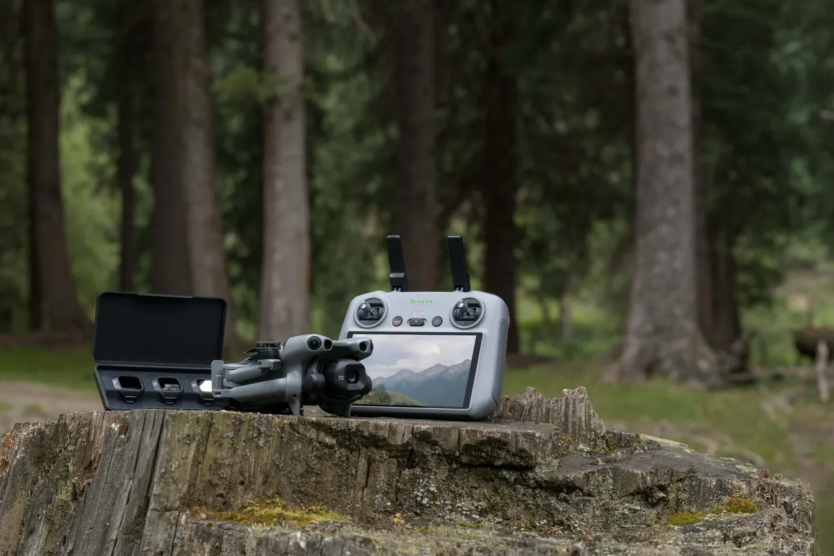 DJI Mini 5 Pro, DJI Mini 5 Pro wraz z aparaturą sterującą i etui, ustawione na pniu drzewa w lesie