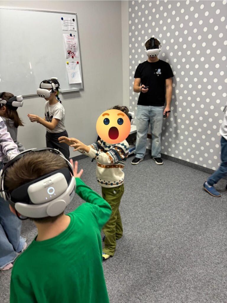 A pupil wearing a VR headset reaching for a virtual object beside the workshop instructor at Harmonia Nieszawska Primary School
