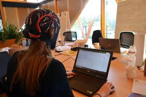 Uczestniczka badania w czepku EMOTIV Flex przy laptopie z zapisem EEG