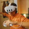 A boy in an orange hoodie using a Meta Quest headset and two controllers