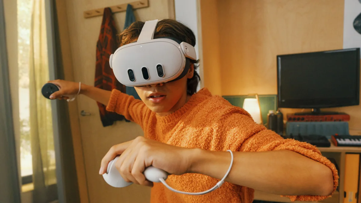 A boy in an orange hoodie using a Meta Quest headset and two controllers