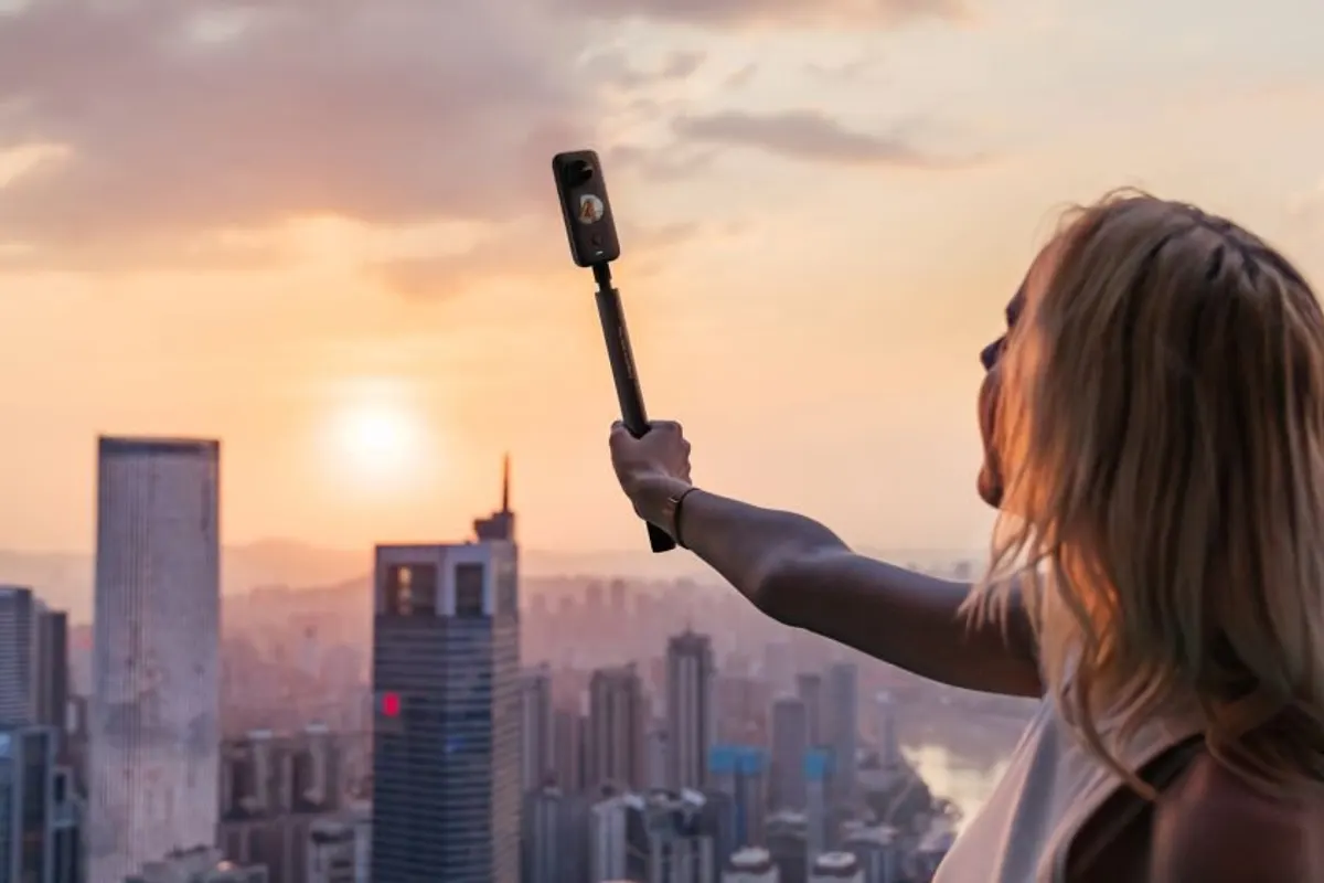 A person holding a selfie stick against a city skyline at sunset